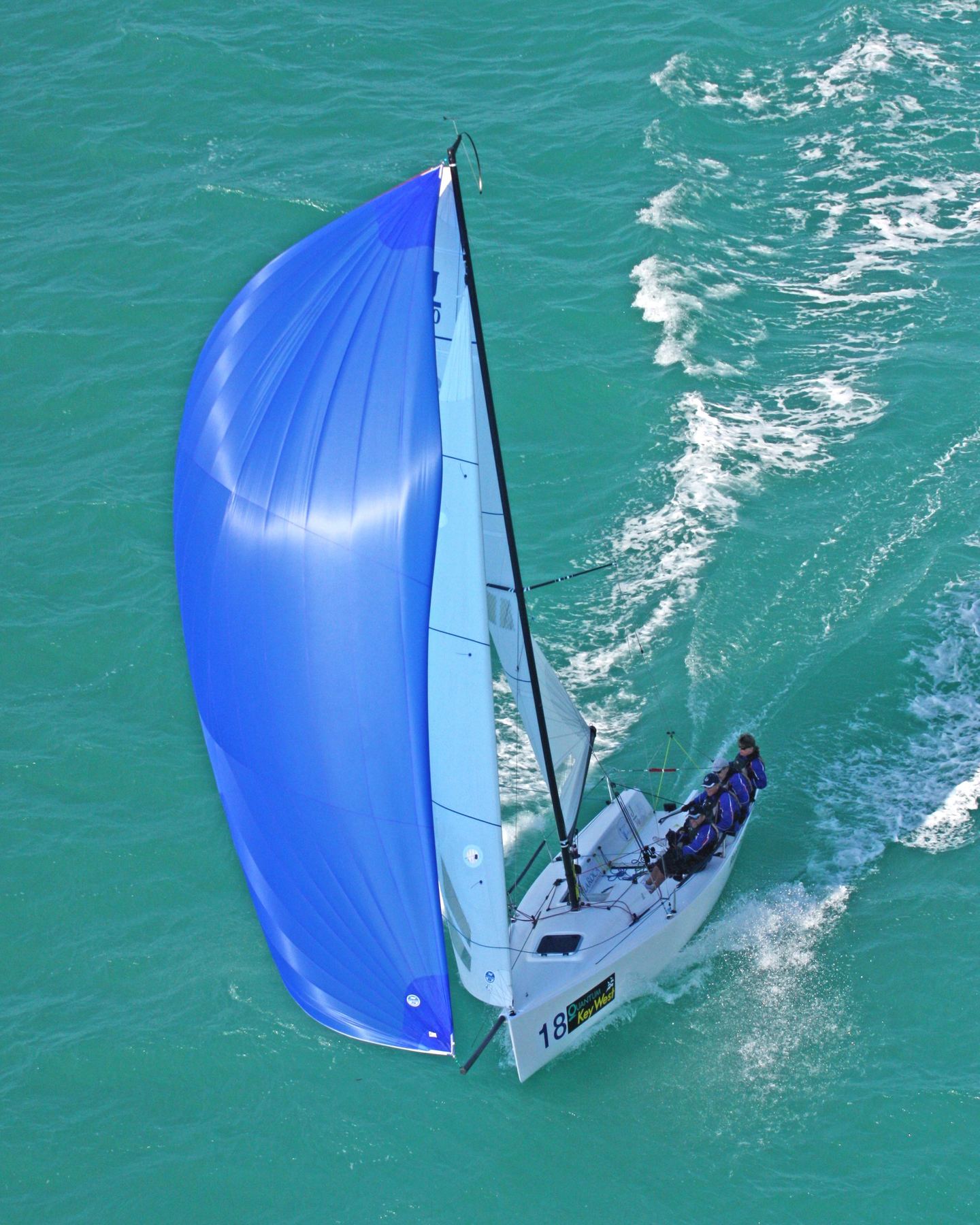 Aerial view of a racing sailboat flying a blue spinnaker over turquoise water